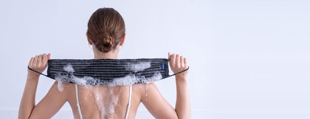 Femme utilisant la serviette exfoliante NORYA sur le dos